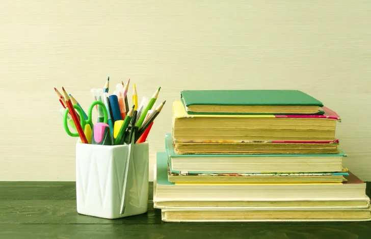 積み上げられた本と四角い容器に入った色鉛筆などの文具