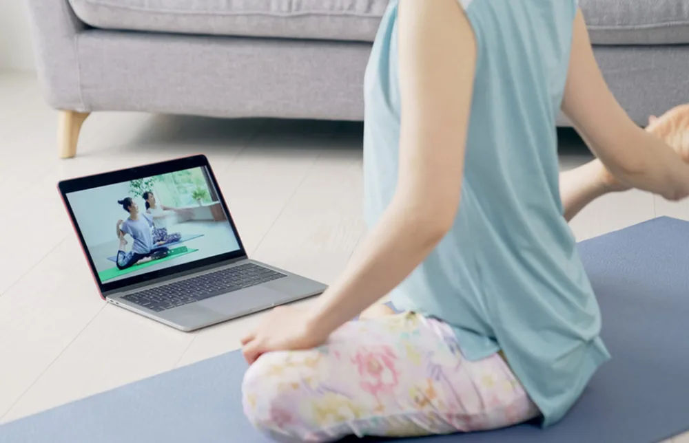 パソコンを見ながらヨガをしている女性