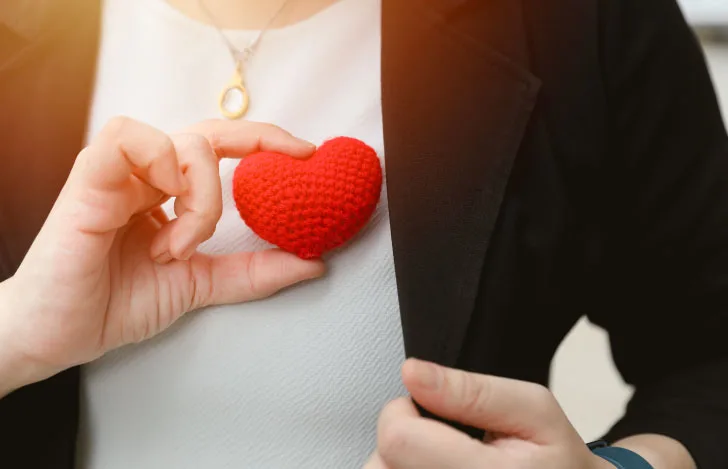 自分の胸にハート型の毛糸のオブジェを当てる女性の胸元