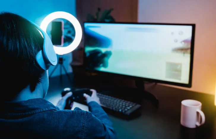 ヘッドフォンを頭につけてコントローラーを手にゲームモニターを見つめる少年の姿