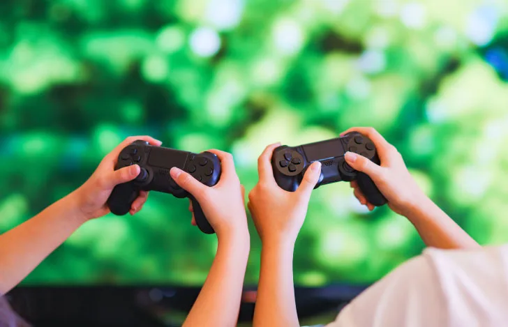 コントローラーを手にゲームモニターに向かう2人の少年の手元