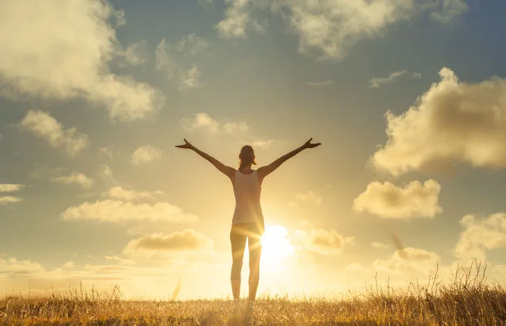朝日に向かって両手を広げて立ち上がる女性