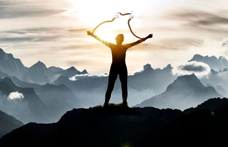 山の頂上で手に繋がれた鎖を断ち切る人のシルエット