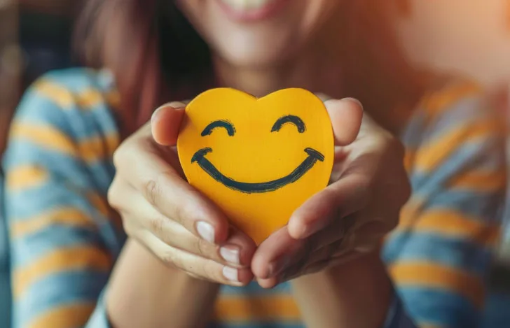 笑顔が描かれたハート型のオブジェを持つ女性の手元