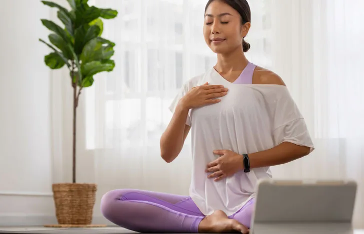 胸とお腹に手を当て座って目を閉じるヨガウェアのきた女性
