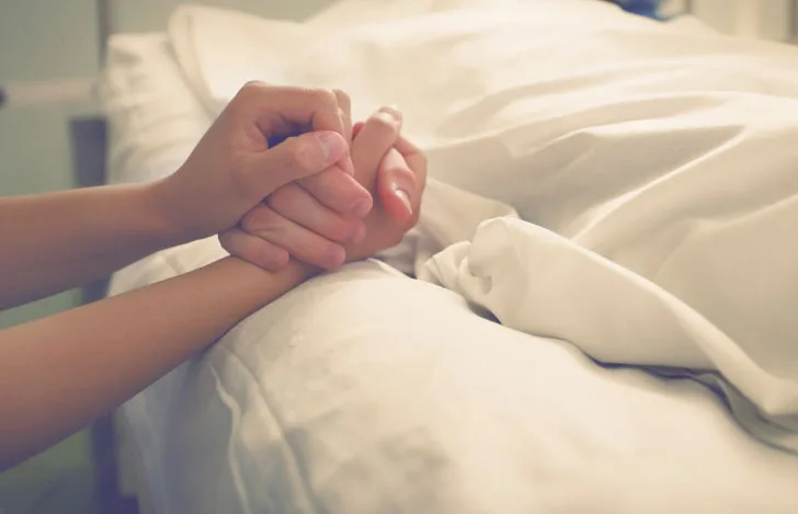 入院ベッドに横たわる人の手を握る様子