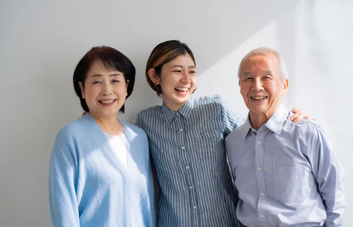 年老いた両親と一緒に笑顔で立つショートカットの女性