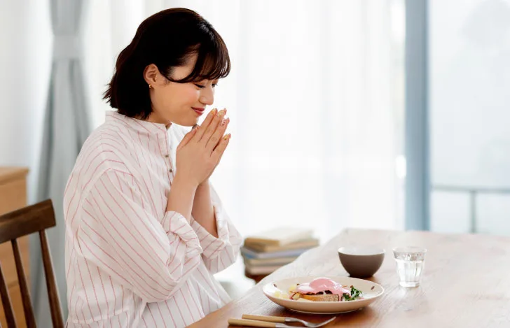 食卓で食事の前に手を合わせて目を閉じる女性