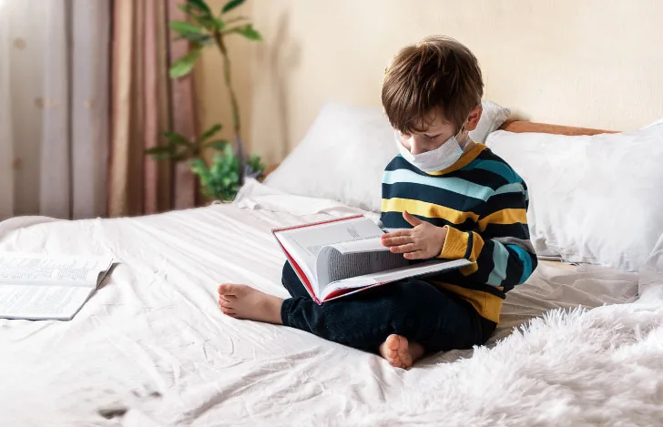 ベッドの上で本を読むマスクをした少年