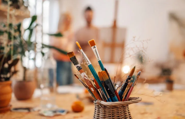 アトリエの中のイーゼルを囲む夫婦とテーブルの上の絵筆が入ったポット