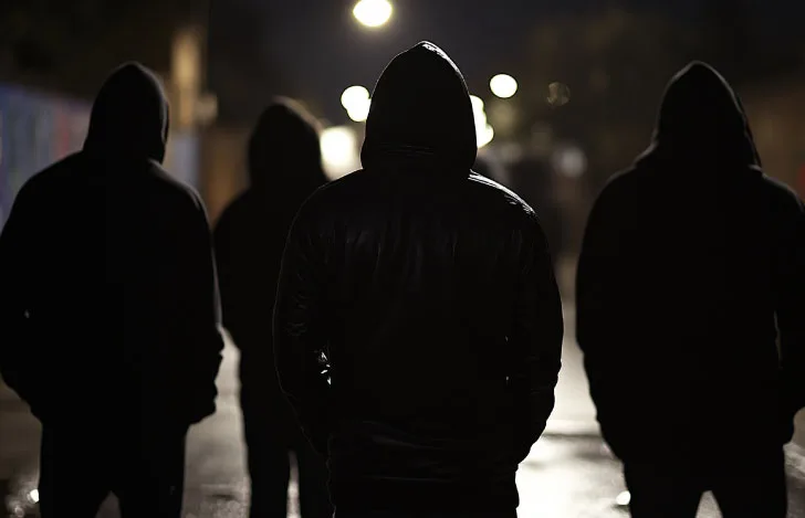 暗い街の街灯を背にしたフードを被った4人の男のシルエット