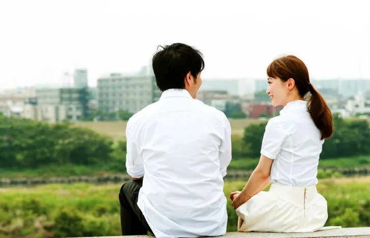 土手に座る2人の男女の後ろ姿