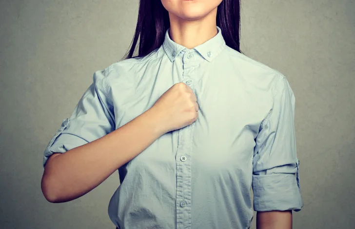 拳を胸に当てるシャツを着た女性