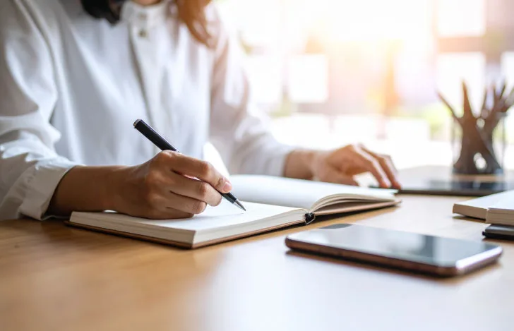 机でノートに何かを書き込む女性の手元