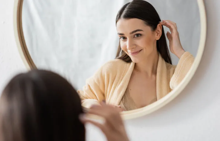 鏡に映る自分を見ながら耳に髪をかける女性