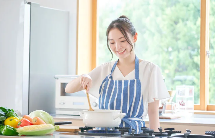 朝日が差し込むキッチンで笑顔で料理する女性