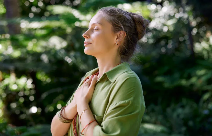 自然の中で目を閉じて手を胸に当てる緑のシャツを着た女性