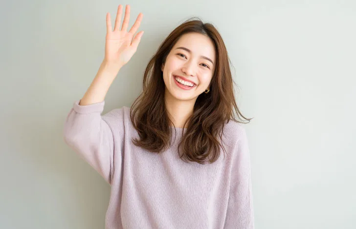 笑顔で片手を挙げる髪の長い女性