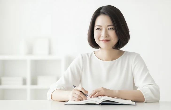 鉛筆を持ってノートに書き物しながら微笑む女性