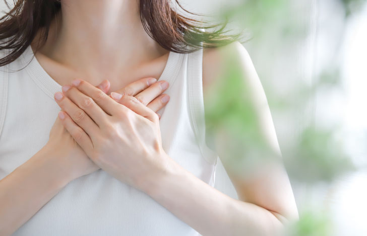 胸に両手を当てる白いタンクトップを着た女性