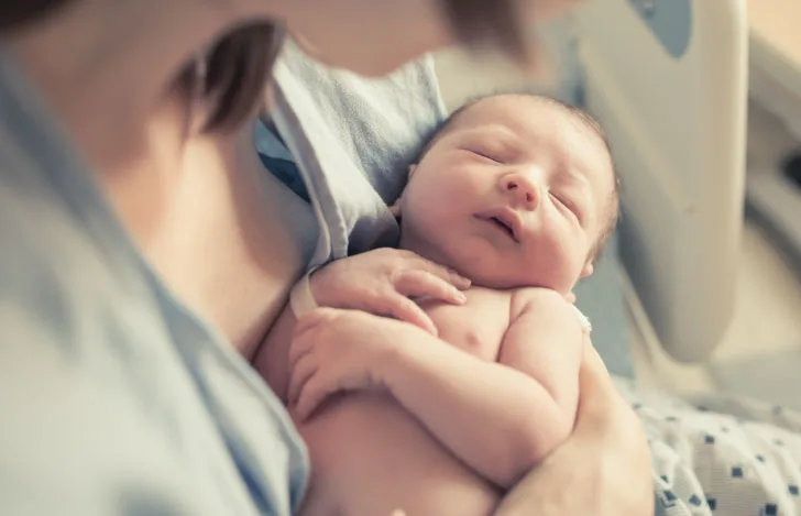 女性の腕に抱かれた生後まもない赤ちゃん