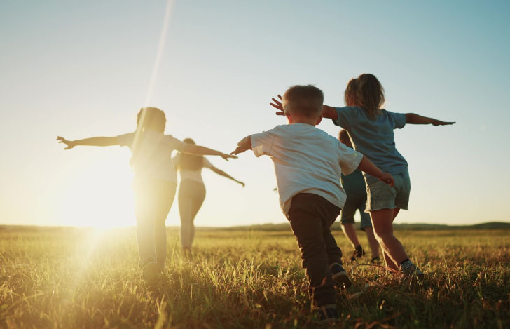 光に向かって草原を走る子供達の後ろ姿