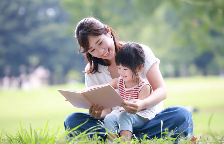 芝生の上で本を読む親子